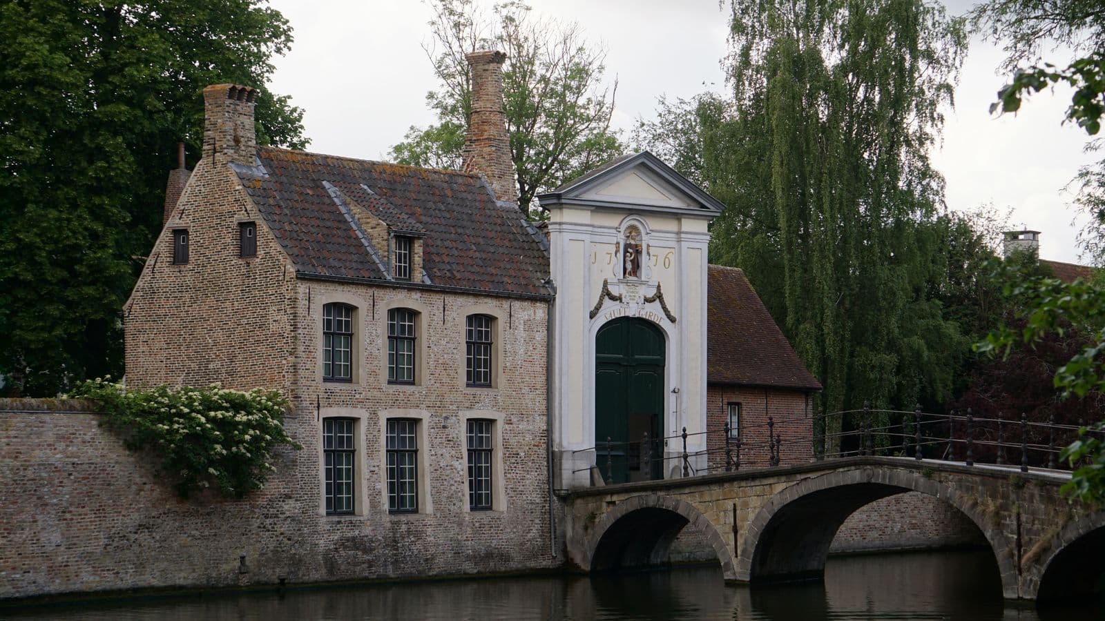 Maison en briques et pont en pierre au bord d'un canal historique à Bruges, illustrant une adresse de siège social pour la domiciliation d'entreprise à Bruges