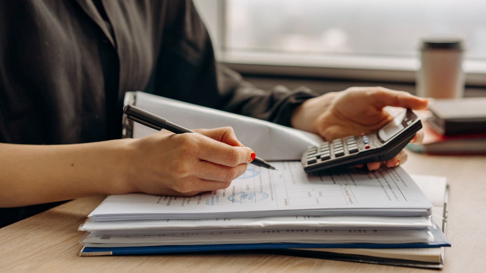 Expert-comptable utilisant une calculatrice et examinant des documents financiers dans un bureau professionnel