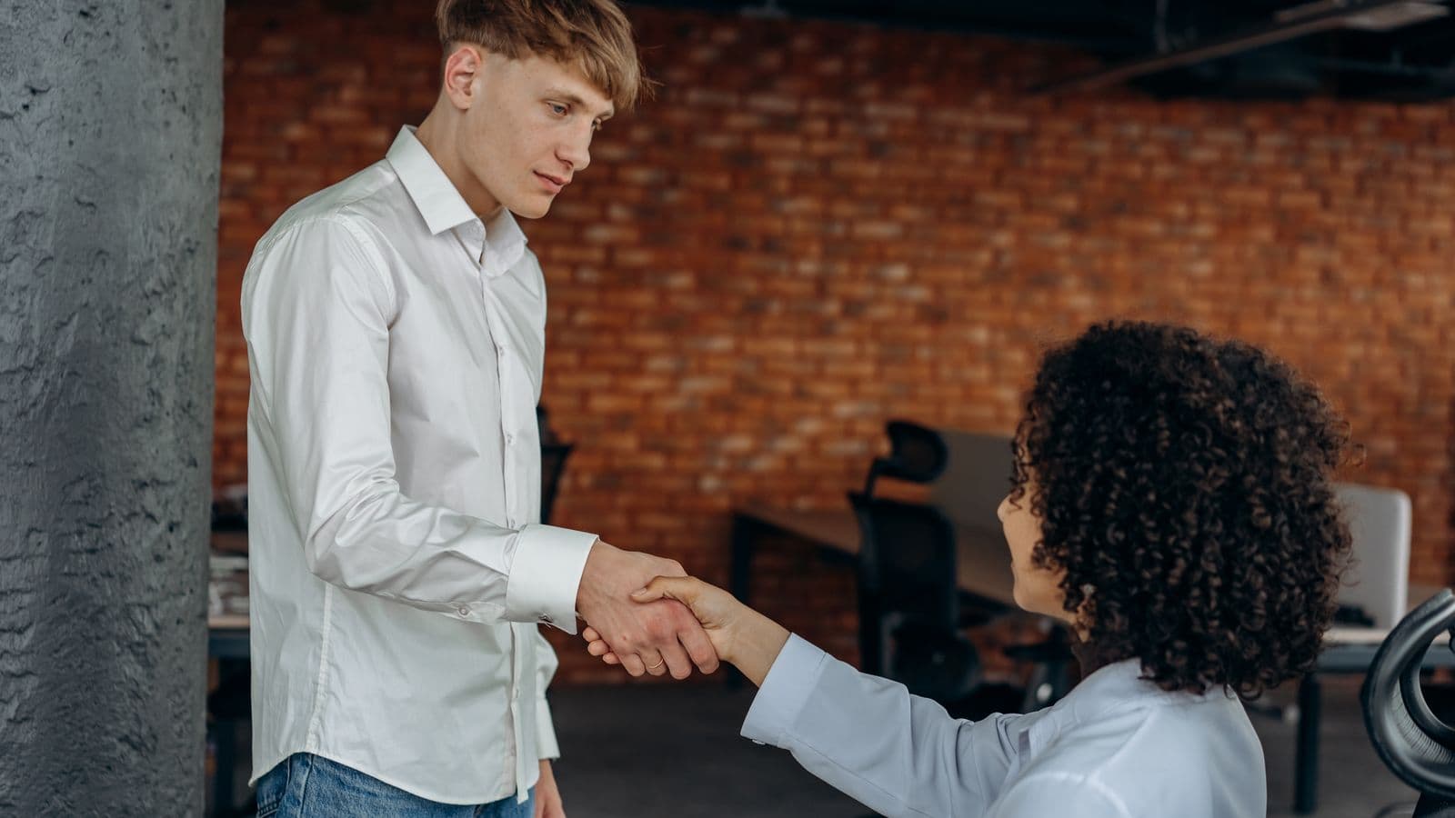 Deux professionnels, une femme et un homme, se serrant la main dans un bureau, symbole d'égalité salariale en entreprise