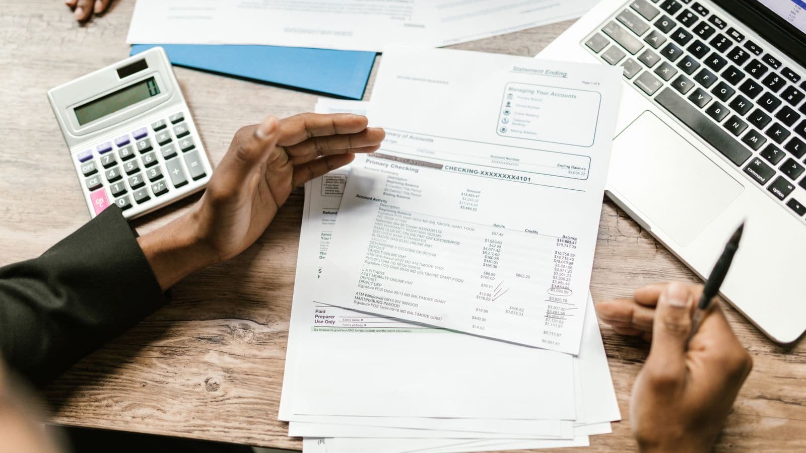 Mains tenant des documents financiers avec calculatrice et ordinateur portable sur un bureau professionnel