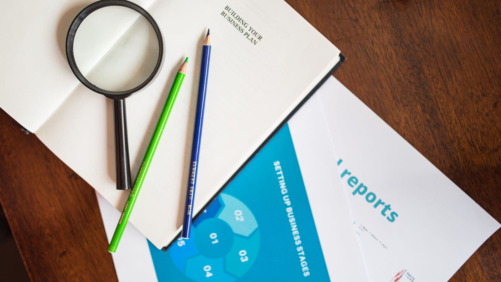 Vue de dessus : loupe et rapports d'entreprise colorés sur un bureau en bois, illustration du rapport de durabilité CSRD