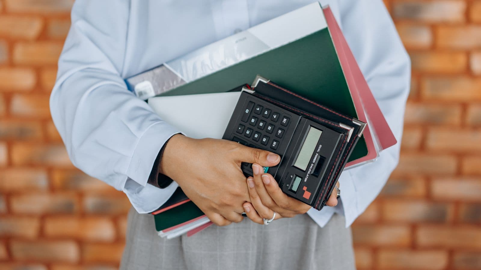 Personne tenant une calculatrice et des dossiers financiers, illustrant le calcul d'une plus-value professionnelle