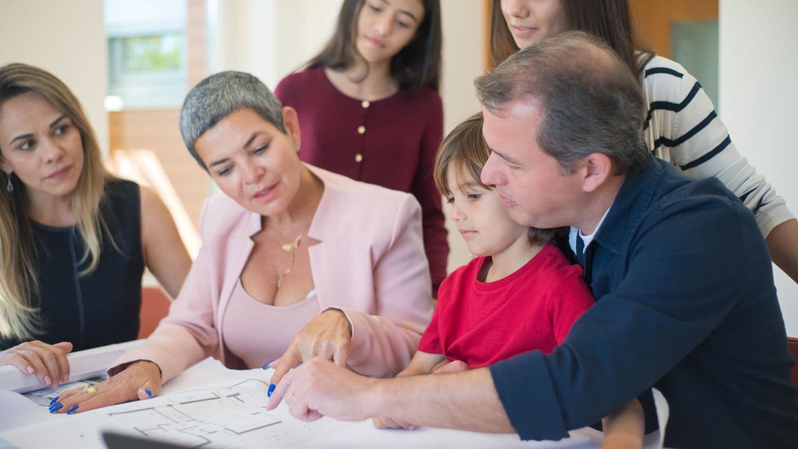 Une famille réunie autour d'une table examine des plans immobiliers avec une conseillère